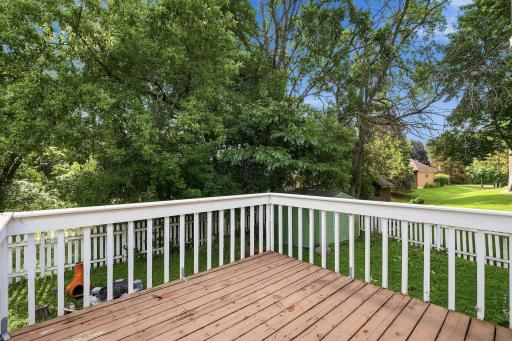 Spacious wooden deck with white privacy railings, offering an ideal outdoor space for grilling, dining, and entertaining while overlooking the backyard trees.