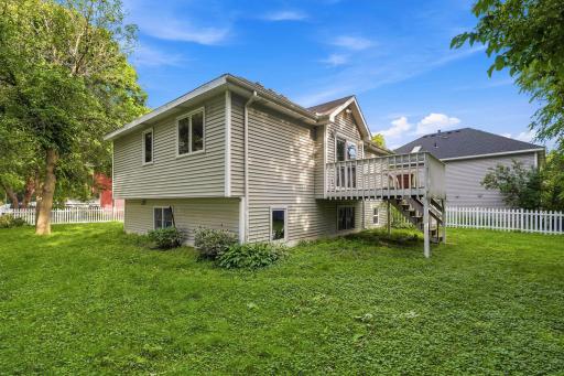 Full view of the home's rear exterior showcasing the elevated walkout wood deck, staircase leading down to the lawn, and clean vinyl siding against a bright blue sky.