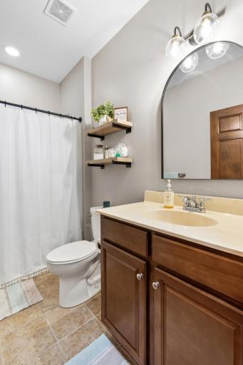 Pristine full guest bathroom upgraded with a modern arched designer mirror, industrial-chic floating display shelving, fresh paint, and flawless knockdown ceilings!