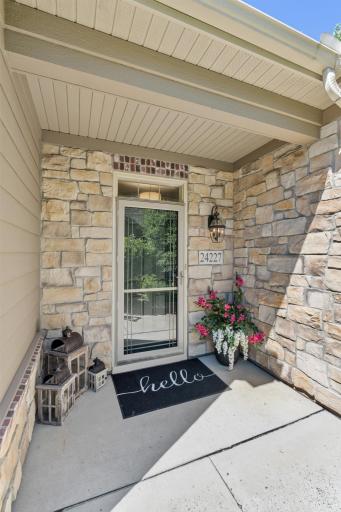 Charming covered front porch entryway showcasing elegant stone accent masonry, a welcoming concrete alcove, and a freshly painted front entry door completed in 2025!