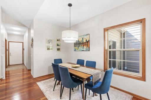 Elegant formal dining room showcasing pristine wood floors, new modern statement lighting, and a clear view of the hallway that leads to the Primary Bedroom, Laundry and Garage Service Door!