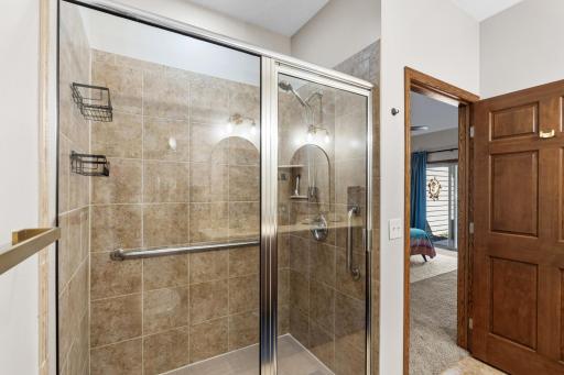 Upgraded primary bathroom showcasing a spacious walk-in tiled shower complete with low-step entry, secure built-in safety grab bars, and a bright glass enclosure!