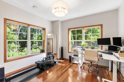 Bright and open dedicated home office area featuring rich wood flooring, crisp contemporary wall paint, exceptional natural light, and a gorgeous new designer light fixture!