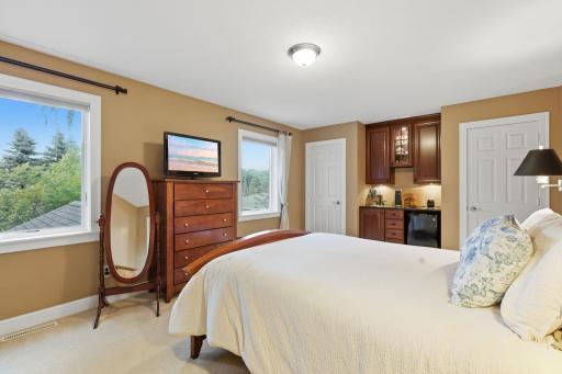 View of the upper level primary bedroom with dual closets a coffee bar and ensuite bathroom.