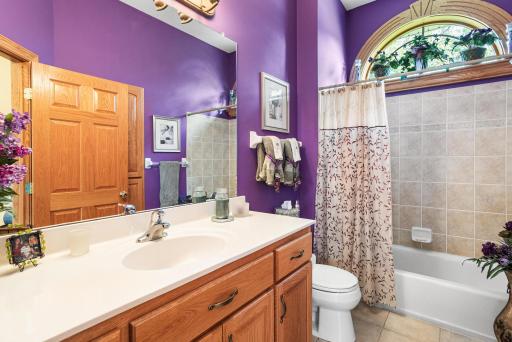 The main-level full bathroom features a spacious vanity, tub/shower combination, tile flooring, and a large arched window that fills the space with natural light.