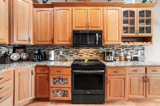 A full wall of cabinetry, granite countertops, tile backsplash, glass-front display cabinets, and built-in wine storage provide generous storage and workspace.