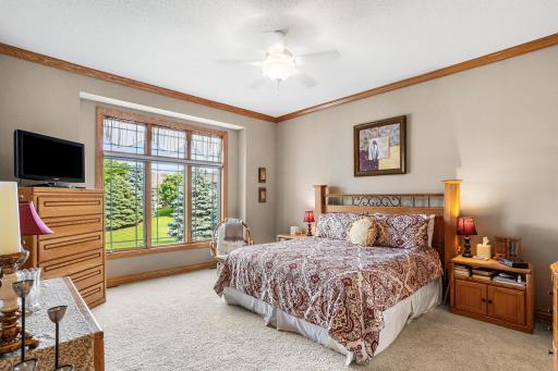 The spacious primary suite features large windows with peaceful backyard and pond views, plush carpet, and generous space for a king-size bed and additional furnishings.