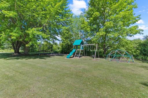 At the rear of the yard, you'll find a play area. An oversized sandbox, trampoline, playset, and climbing sphere are included in the sale price.