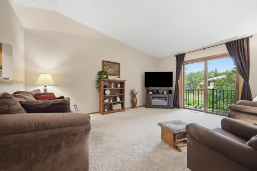 Spacious living room with vaulted ceilings and access to a private deck overlooking mature trees and green space