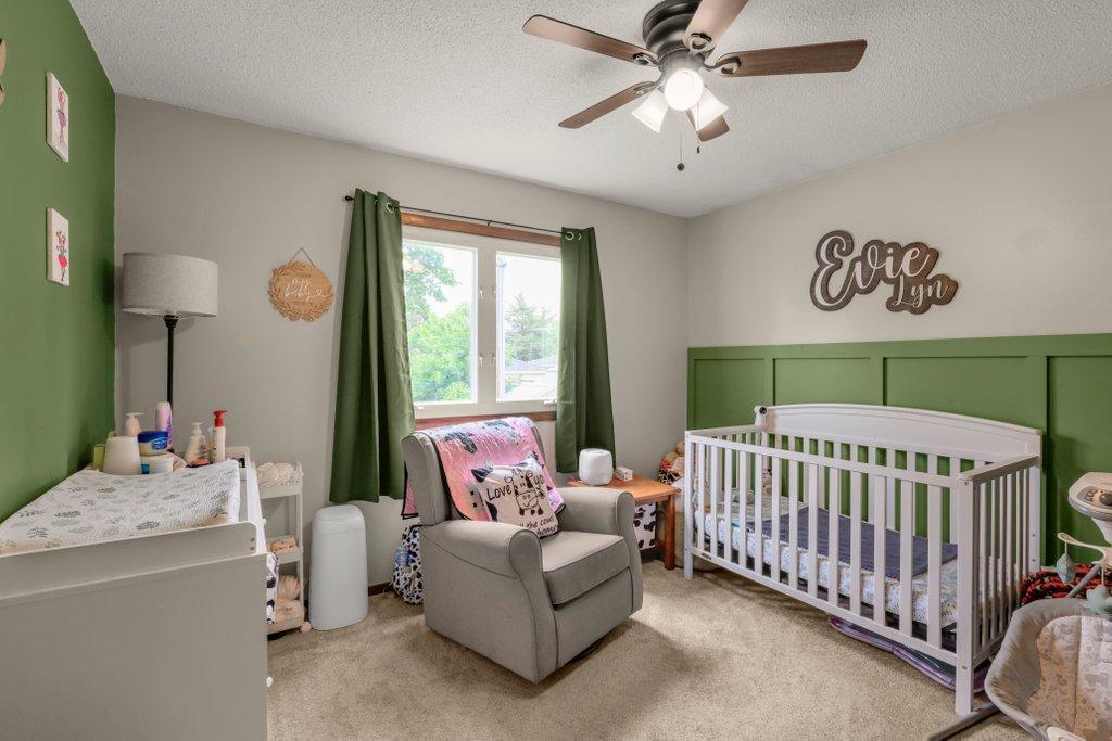 Bright and inviting main-level bedroom featuring designer accent walls, large window for natural light, plush carpet, and flexible space perfect for a nursery, home office, or guest room.