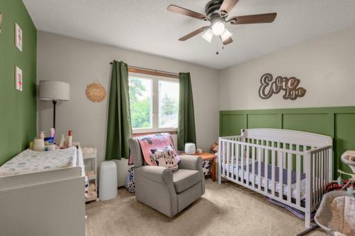 Bright and inviting main-level bedroom featuring designer accent walls, large window for natural light, plush carpet, and flexible space perfect for a nursery, home office, or guest room.
