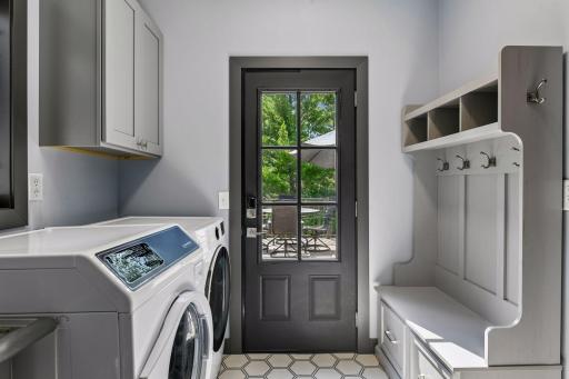 The remodeled laundry and mudroom entry from the garage features a glass-panel exterior door, side-by-side washer and dryer, built-in lockers with bench seating, and upper cabinetry for storage.