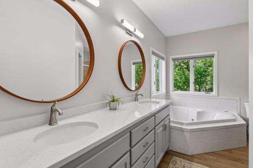 The remodeled primary bath offers a dual-sink vanity, two framed mirrors, and a deep soaking tub