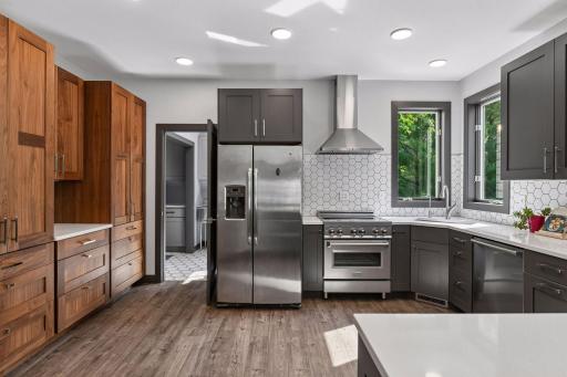 The fully remodeled kitchen offers rich cabinetry, a tile backsplash, stainless steel appliances, and generous prep space beneath windows overlooking the trees.