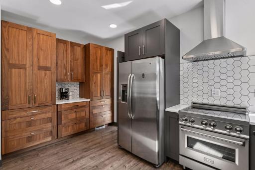 The remodeled kitchen features rich wood cabinetry, a professional-style range, stainless steel appliances, and a tile backsplash with generous counter space.