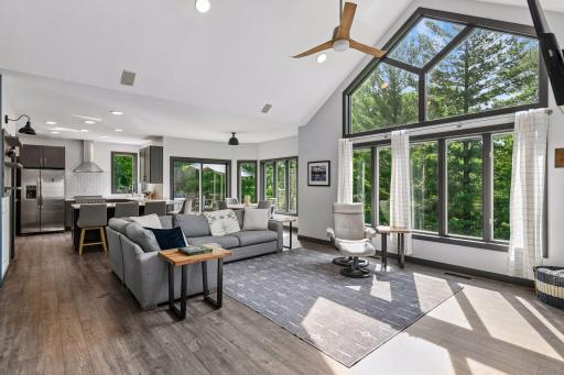 Vaulted ceilings and floor-to-ceiling windows bring natural light into the main living space, anchored by a fireplace and flowing into the kitchen and dining area.