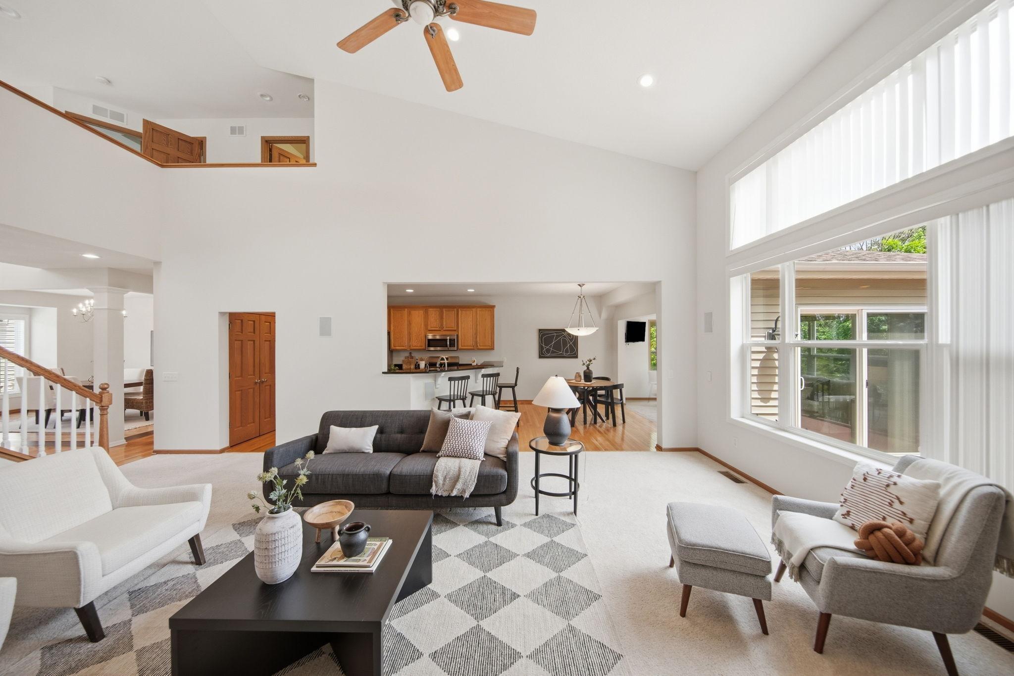 A stunning main-floor family room features soaring vaulted ceilings, a ceiling fan, cozy gas fireplace, and luxurious plush carpeting. Exceptionally spacious and bathed in natural light, this inviting room is ideal for both relaxing and entertaining.