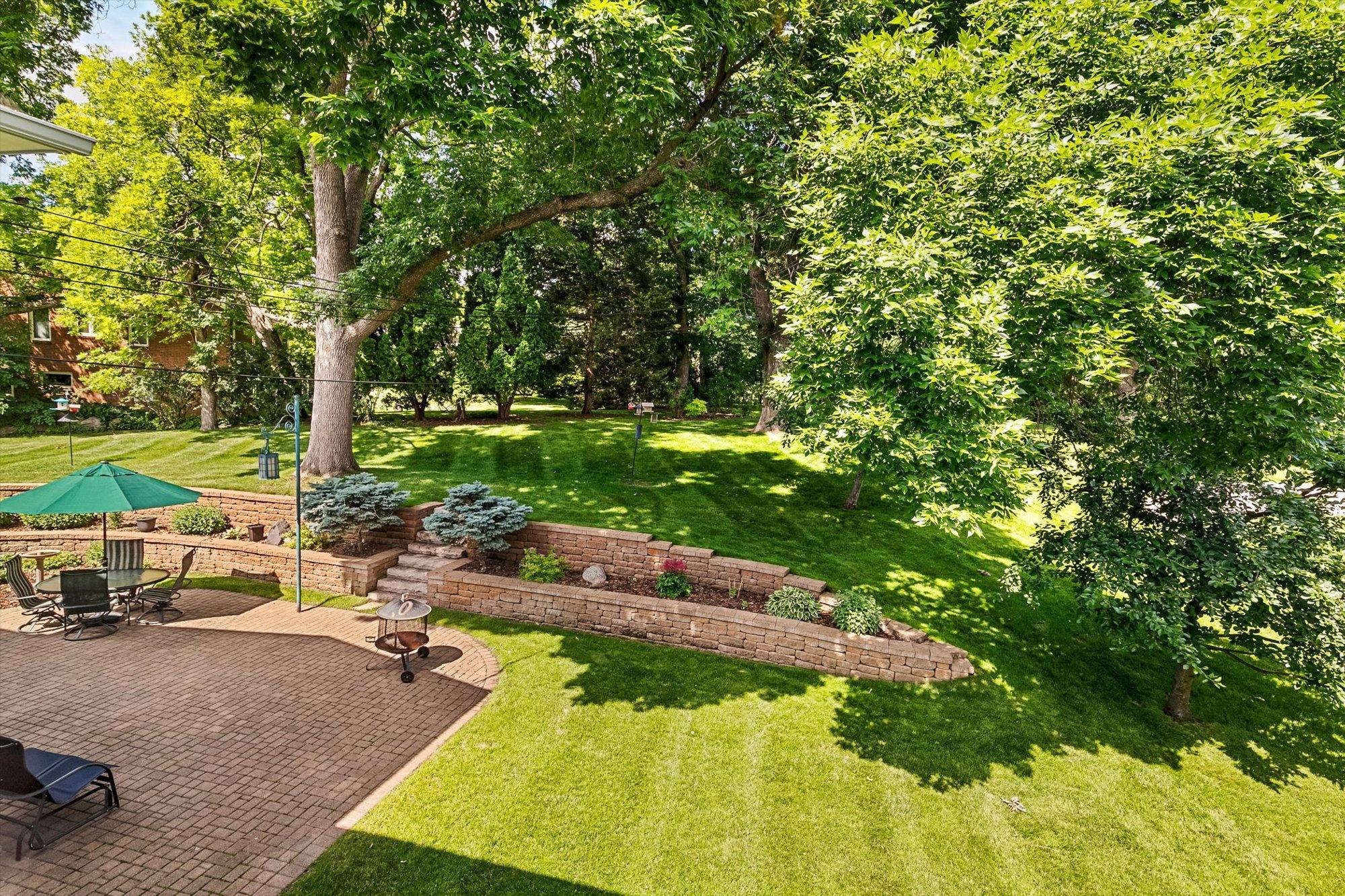 Rear yard space offers a large, entertainment sized, paver brick patio, stone retaining wall that houses featured perennials and lush growth that provides for color year around. Note the expansive rear yard spaces.