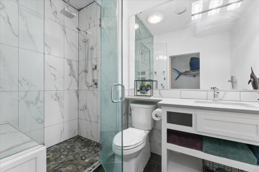 Impressive shower with floor to ceiling custom glass enclosure and pivot-panel to experience a true steam shower. Luxurious rainfall showerhead as well as hand wand, built-in seat, mosaic pebble floor and tile to the ceiling.