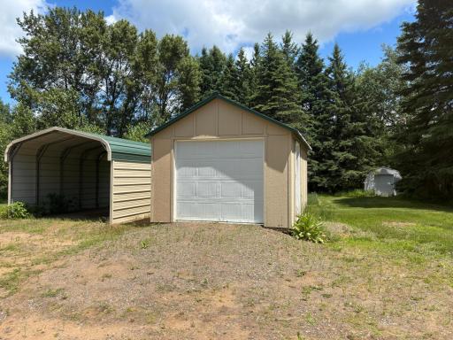 On the left sits a 12x20 metal carport. On the right is a wood framed shed measuring 12x16 and has wood floor and smart siding. All buildings have metal roofs.