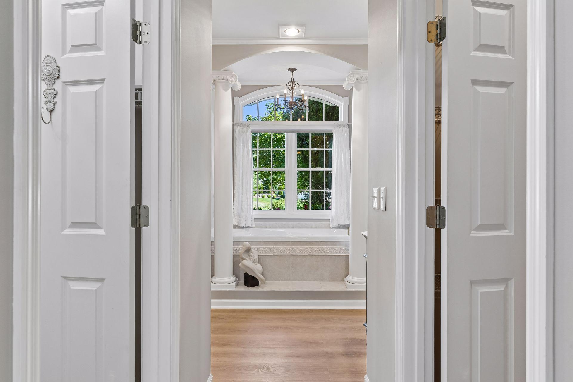 A luxurious Owner's Bath with heated floors, Quartz countertops, a soaking tub framed by decorative columns, and a beautifully tiled walk-in shower.