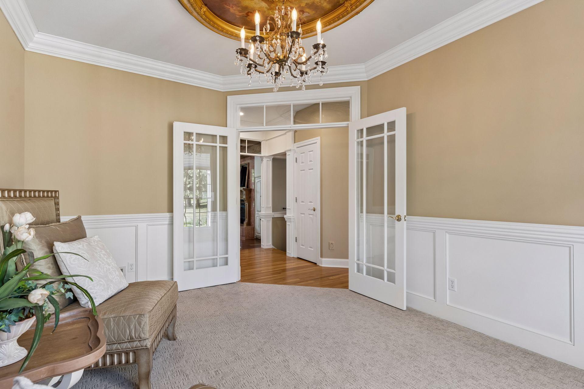 Another view of the Living Room with elegant white paneled walls, extensive Crown Molding, and French doors.