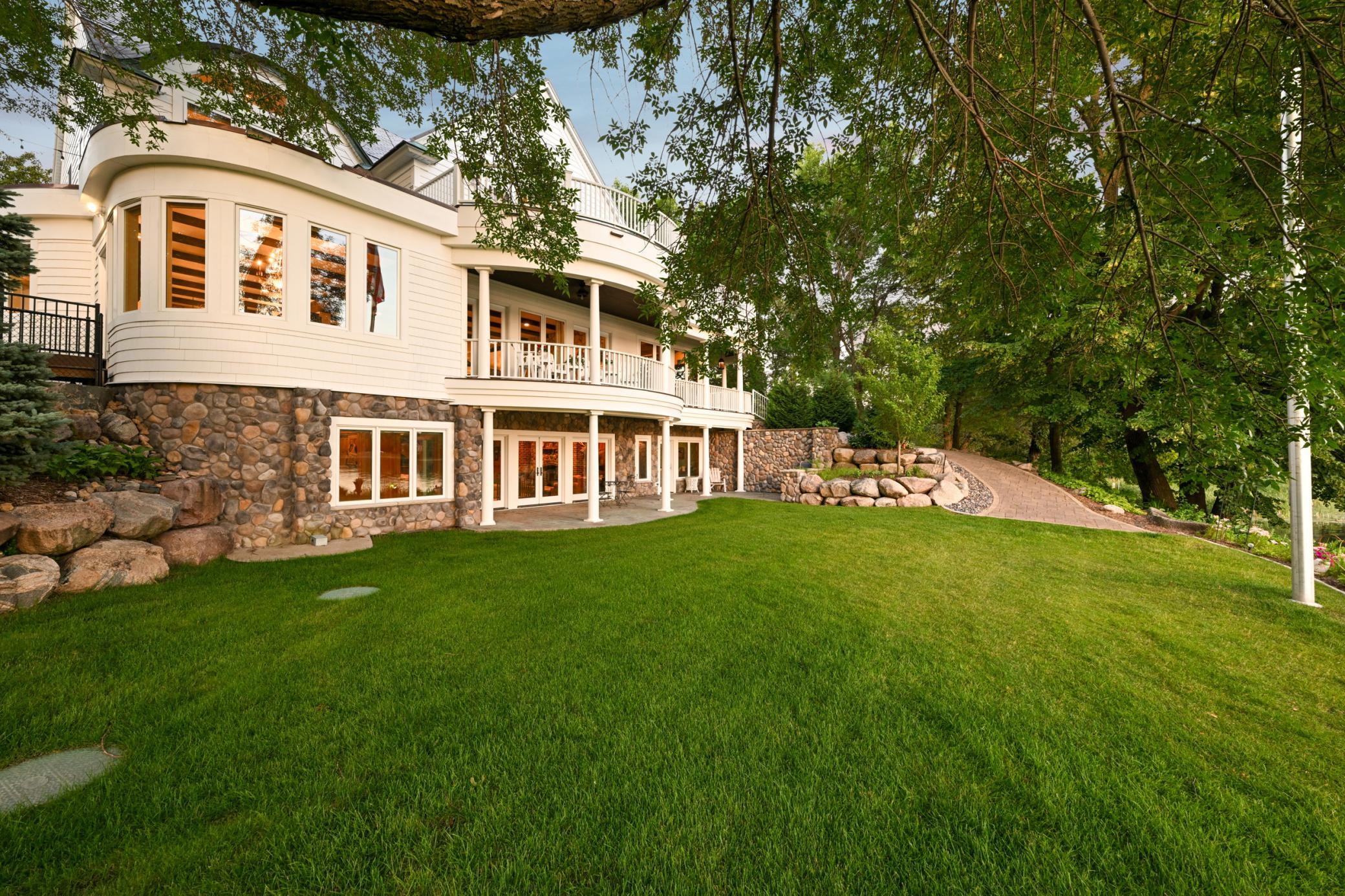 The walkout lower level opens to a lush, manicured lawn, while the upper-level balcony offers sweeping views and elegant outdoor living space. Thoughtfully landscaped with paver pathways leading you to the lake without stairs.