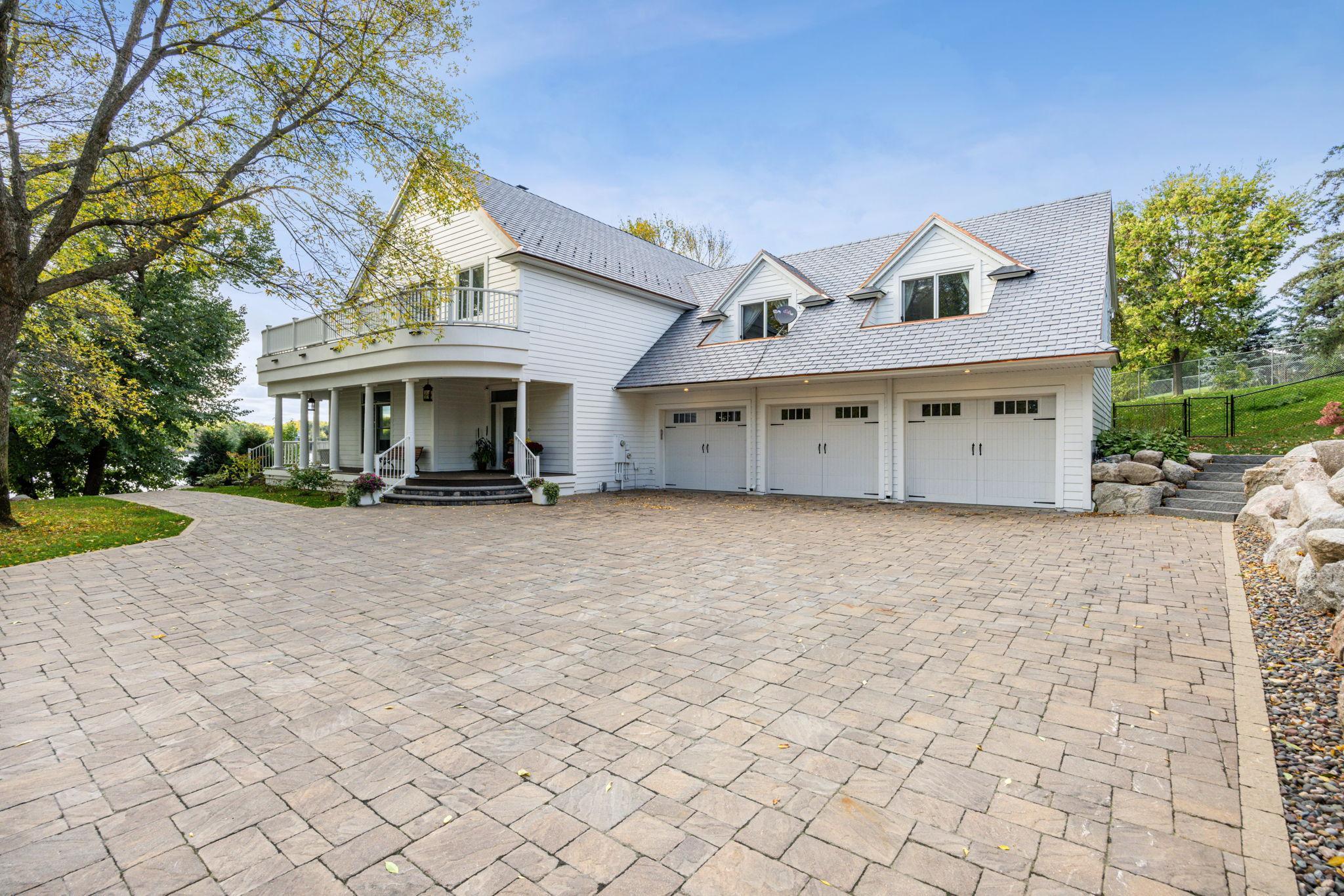 Impressive front elevation featuring a heated paver driveway, charming wraparound porch, and oversized three-stall garage. Classic architectural details and manicured grounds set the tone for this exceptional lakeshore estate.