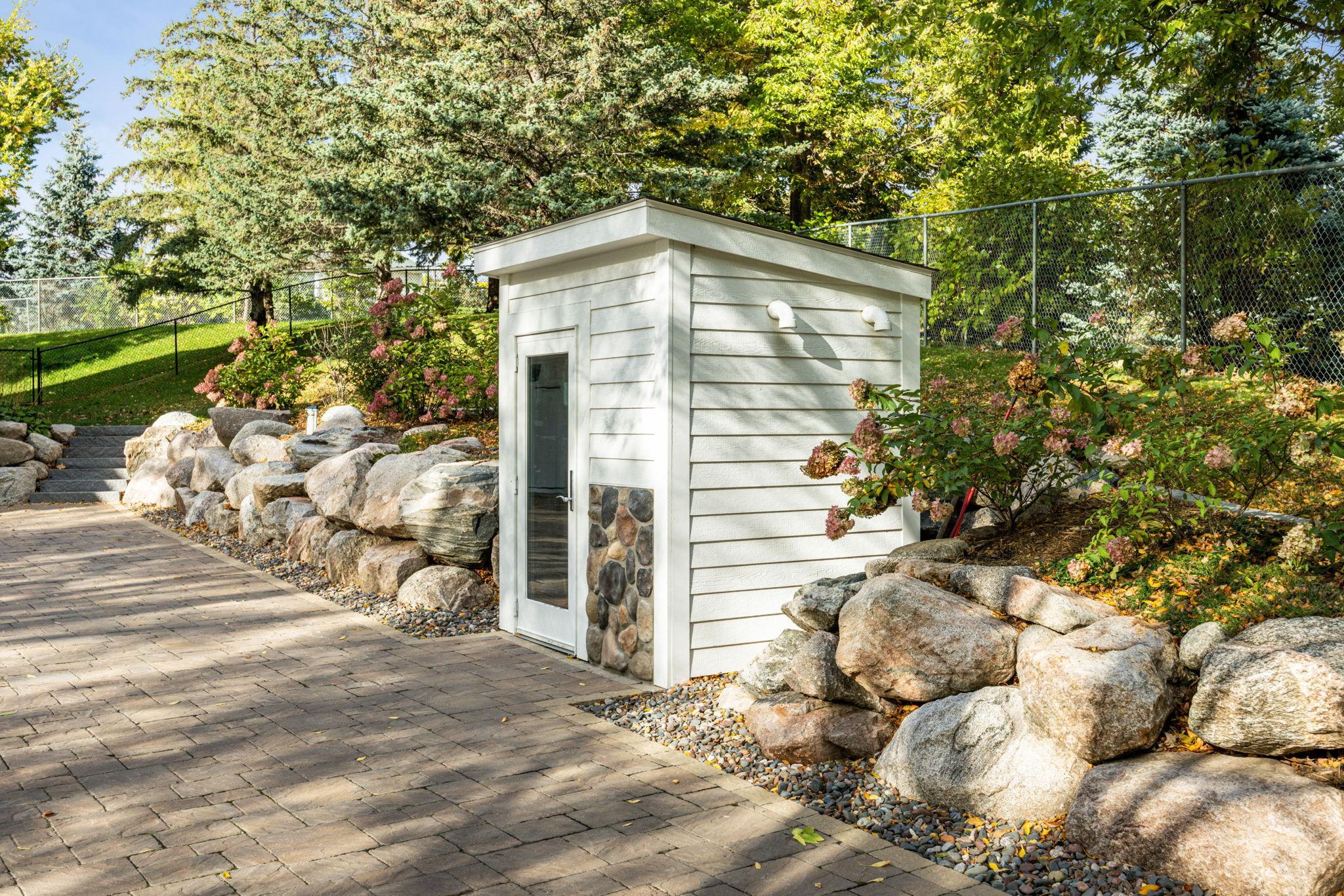 Discreetly tucked into the landscape, this custom utility shed houses the mechanical systems for the heated paver driveway. Thoughtfully designed to blend with the home's exterior, it ensures year-round convenience without compromising aeshetics.