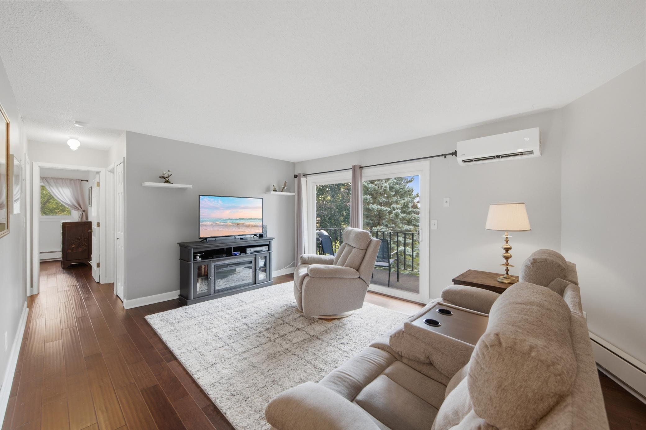 The sunlit living room has access to the balcony through the sliding glass door.