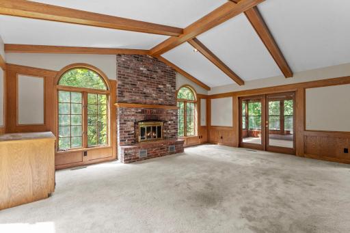 Vaulted and solid beams in main floor living room with brick fireplace, flanked by sizable screen porch or the other side is deck space.