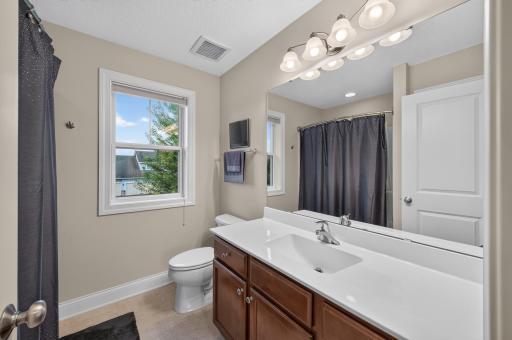The well-appointed upper level guest bathroom features a large vanity, generously sized mirror, and a window that fills the space with natural light.