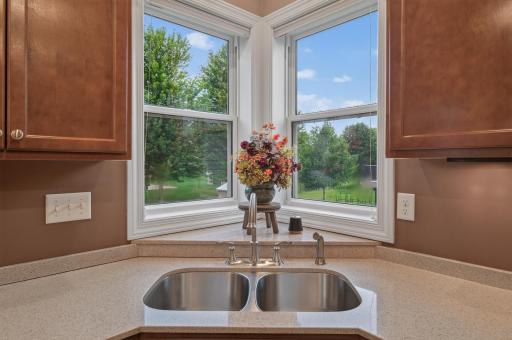 Framed by oversized corner windows, the kitchen sink overlooks a peaceful backyard setting, bringing natural sunlight and scenic views into your daily routine.