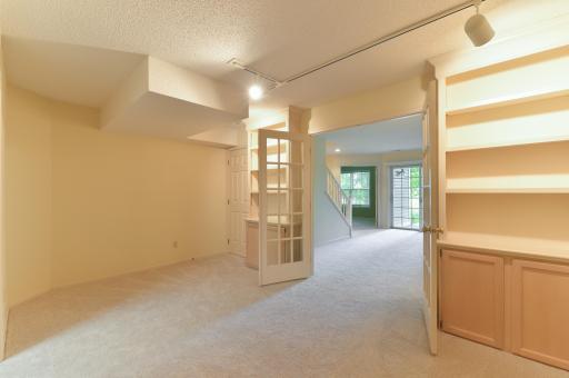 Versatile lower-level bonus room with French doors and built-in cabinetry and shelving.