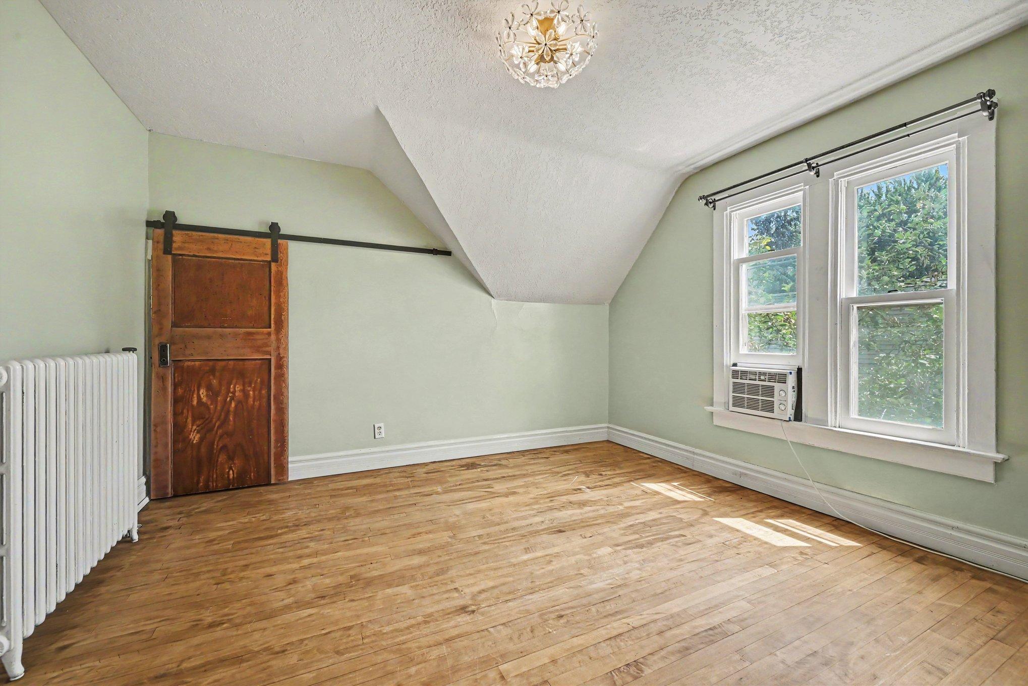 Behind the barn door is an unfinished attic for storage. This second bedroom has great natural light and beautiful hardwood floors.