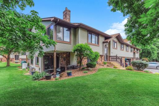 Attractive side elevation showcasing the home's corner lot, mature trees, and beautifully maintained landscaping. Large windows provide abundant natural light, while the covered lower-level patio offers a comfortable outdoor retreat.