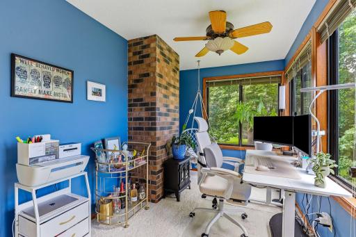 Versatile sunroom/home office featuring walls of windows with peaceful views of mature trees and green space. A striking brick accent wall adds character, while the bright, comfortable setting makes an ideal workspace, reading room, or sitting area.