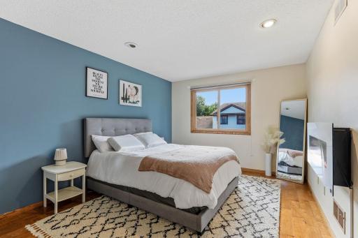Spacious primary bedroom featuring luxury vinyl plank flooring, a large window for natural light, and a stylish accent wall.