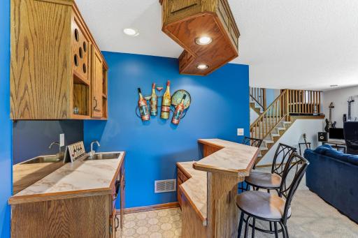 Lower-level wet bar featuring oak cabinetry, a sink, built-in wine storage, and bar-top seating.