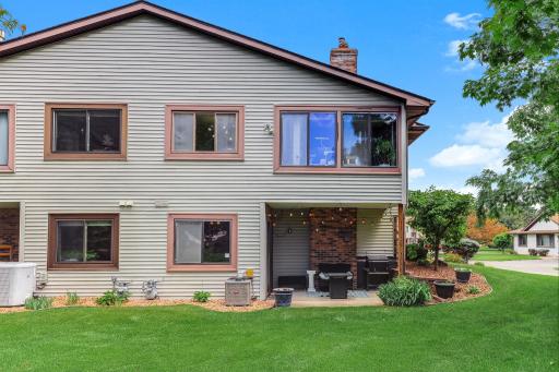 Rear exterior view showcasing the covered patio, walkout lower level, and expansive green space. Mature trees, well-maintained landscaping, and open lawn areas create a peaceful setting with plenty of room to relax, entertain, and enjoy the outdoors.