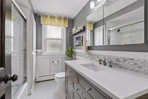 Main floor full bathroom with quartz countertops, tiled floor and white trim/wainscoting, newer fixtures.