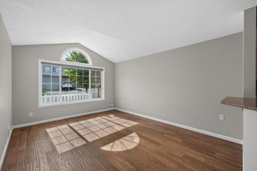 Vaulted living room highlighted by soaring ceilings, hardwood floors, and an oversized arched window that fills the space with natural light.