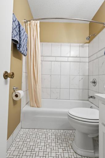 Full Bath with new ceramic tiles on walls. The bathroom carries a tranquil, understated beauty. Crisp white surfaces and subtle marble-patterned tiles reflect the light softly, creating an atmosphere of stillness and clarity