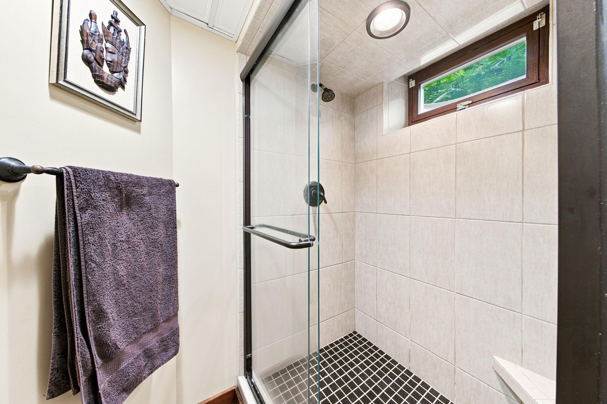 Fully tiled shower with glass enclosure, shower light & transom window that provides daylight