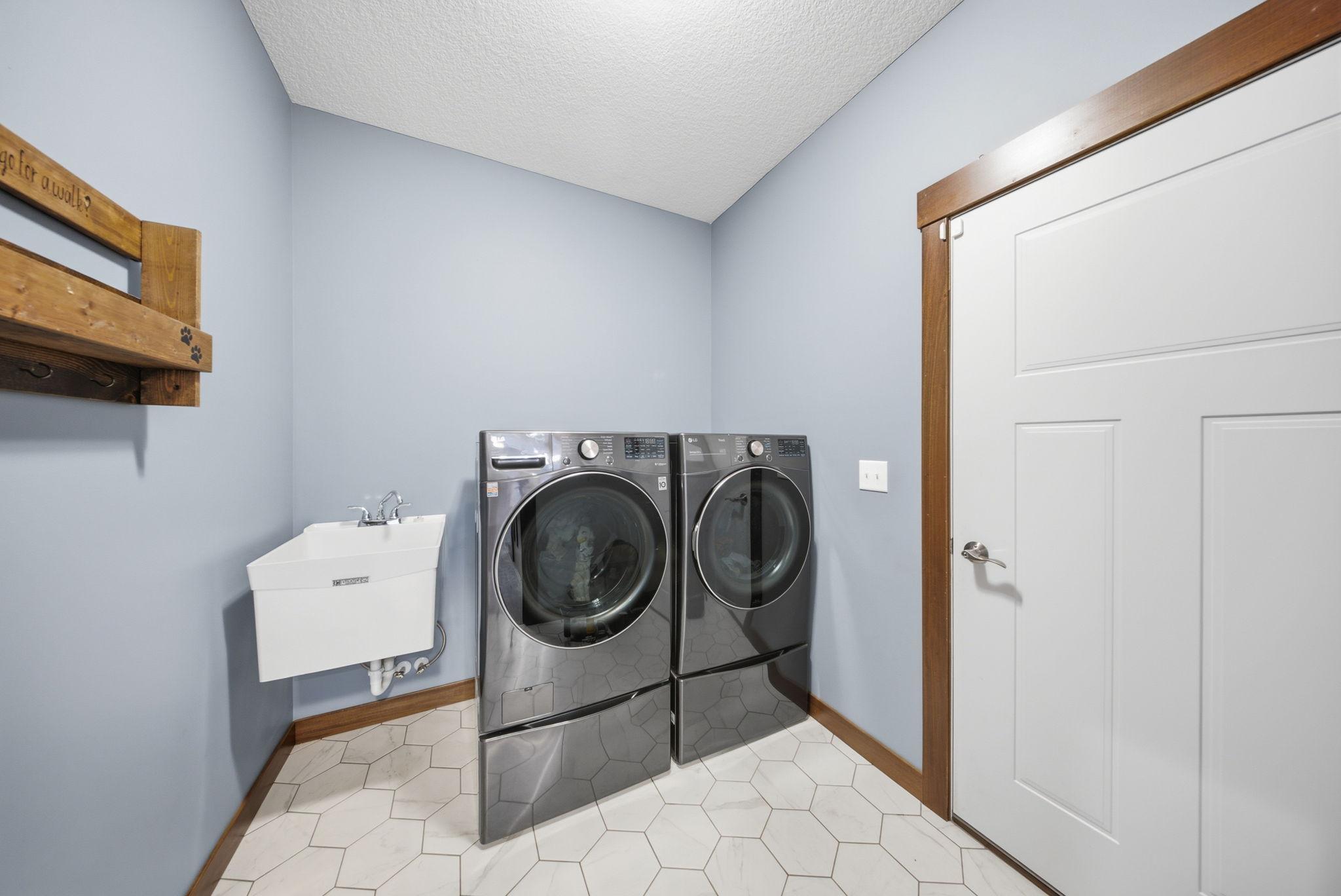 Spacious main-level laundry room with utility sink, durable tile flooring, and generous storage space.