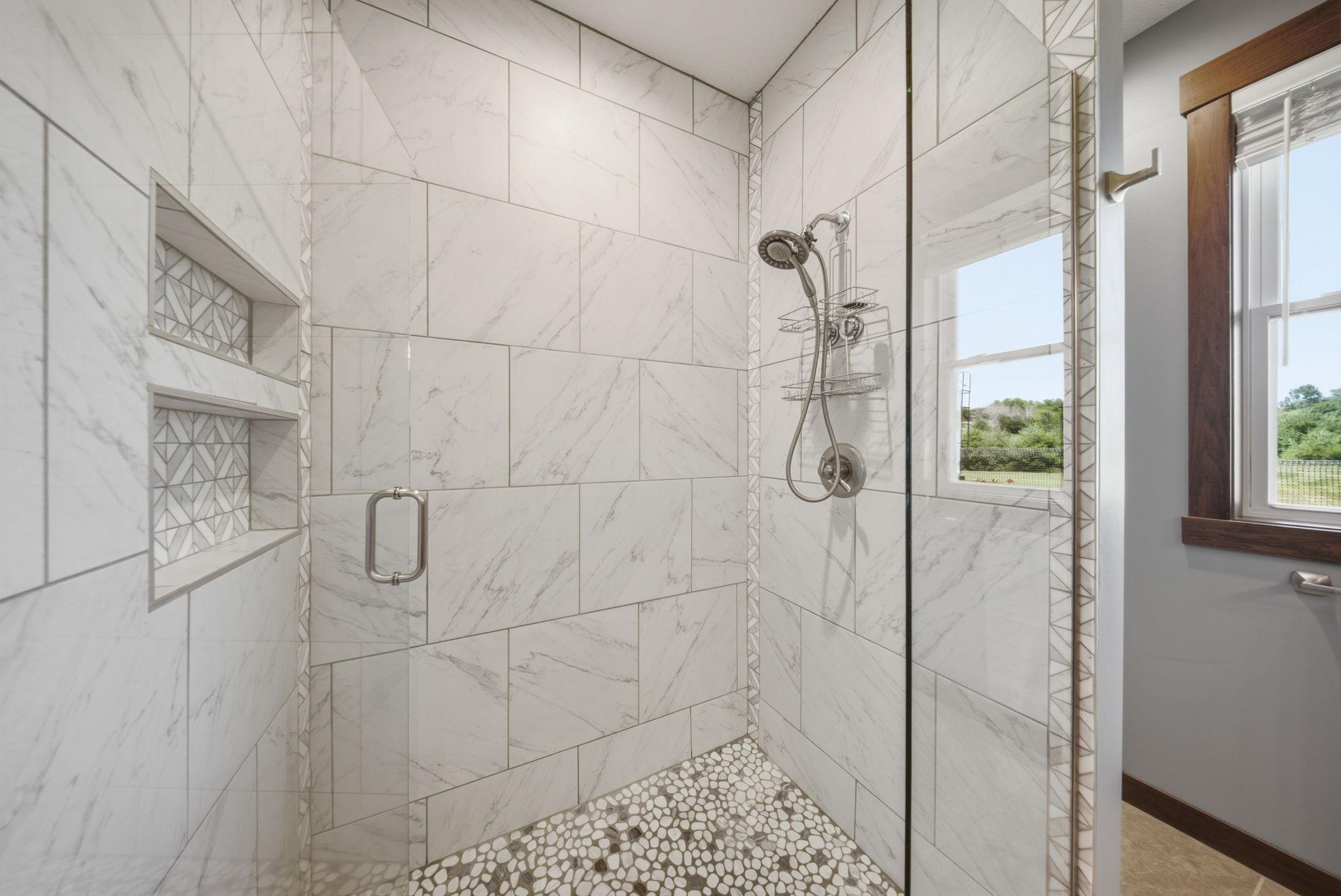 Beautifully tiled walk-in shower with glass enclosure and built-in storage niches.