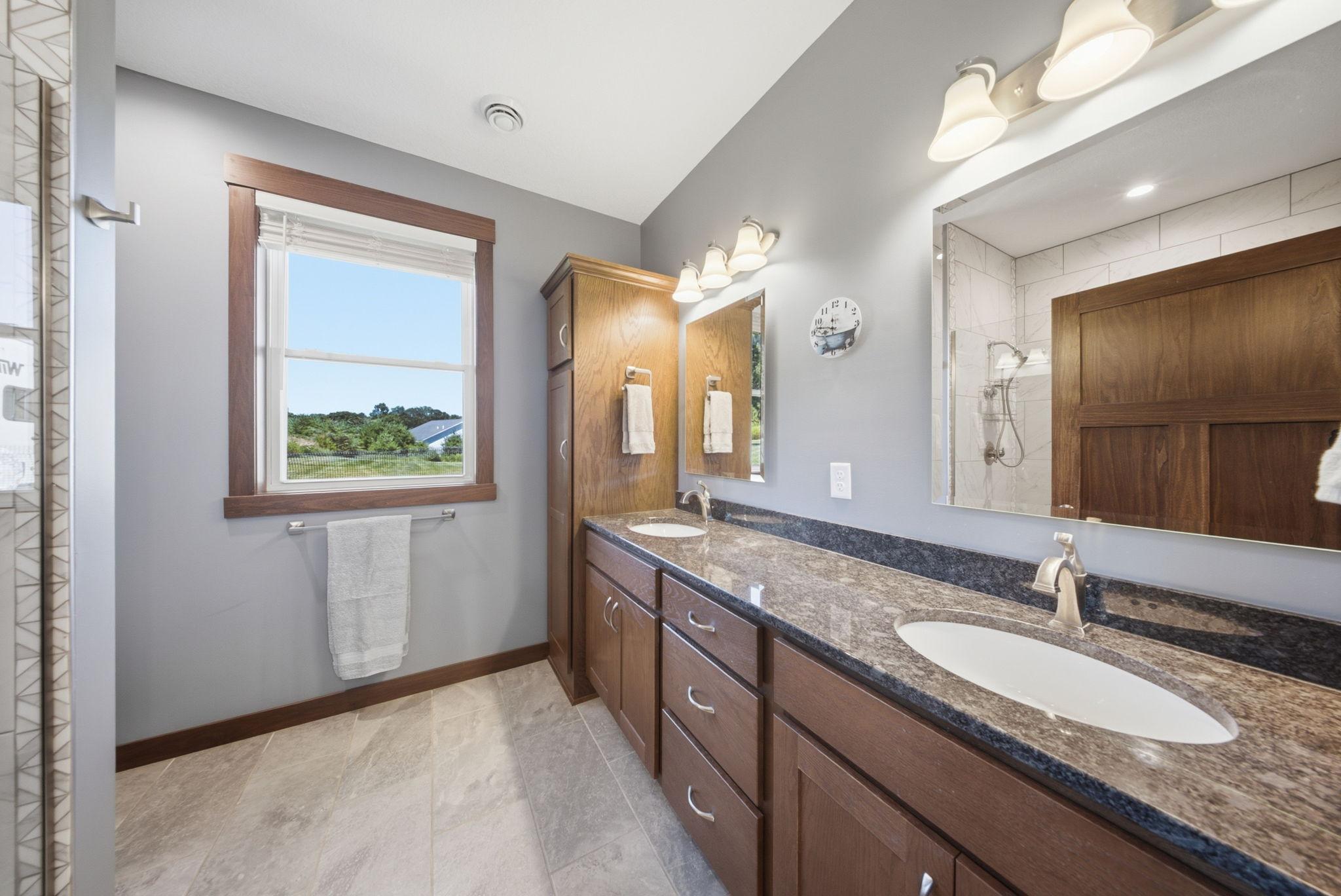 Private ensuite bath with double vanity, granite countertops, and custom tiled walk-in shower.