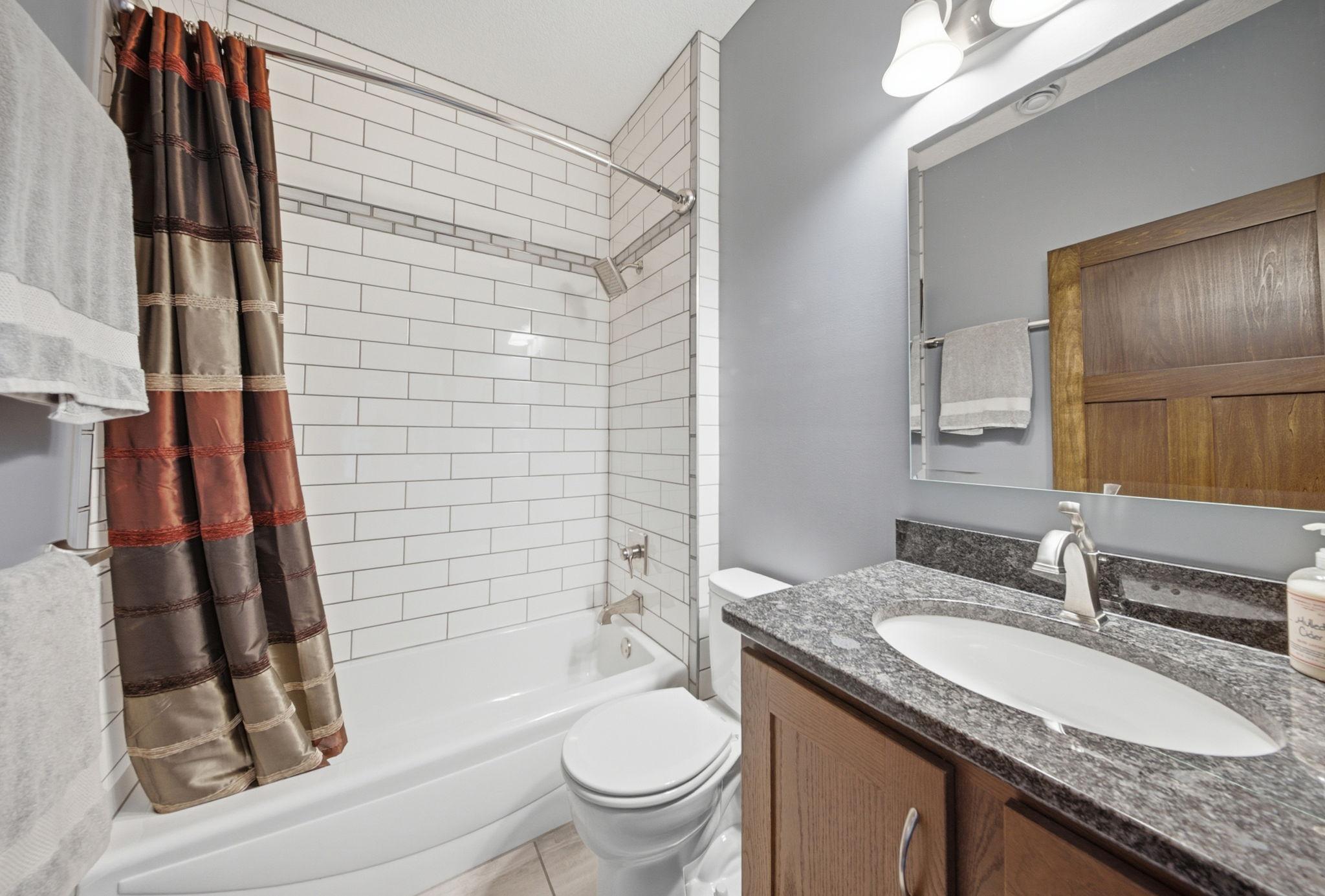 Full bathroom with granite vanity and tiled tub/shower surround.