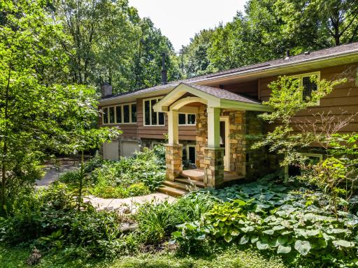 A stone-accented front entryway, nestled within perennial gardens and mature trees.