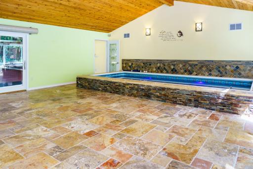 Features heated travertine tile floors for year-round comfort, a custom stone pool surround, and another sliding door providing direct access to the outdoor spa.
